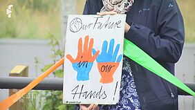 Hände halten ein bemaltes Plakat, darauf sind 2 Hände zu sehen und der Text "Our future in our hands"