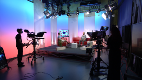 Blick in ein Fernsehstudio mit 2 Kameras, einer roten Couchgarnitur und zwei Talkgäste