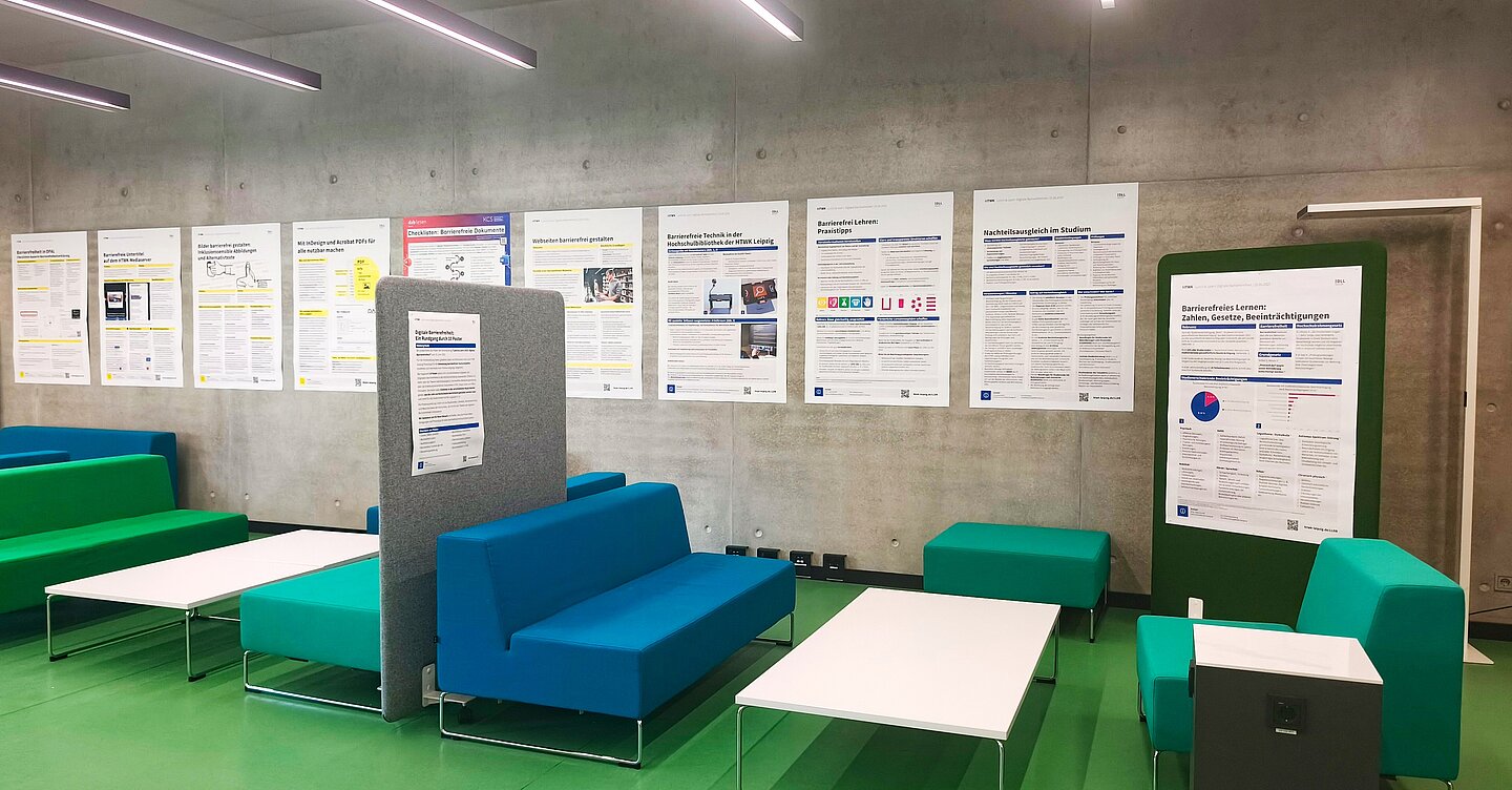 an einer grauen Betonwand sind Poster in Größe A0 in einer Reihe aufgehangen, davor sind Sitzmöbel, Tische und Trennwände zu sehen, die zum öffentlichen Arbeitsbereich der Hochschulbibliothek gehören