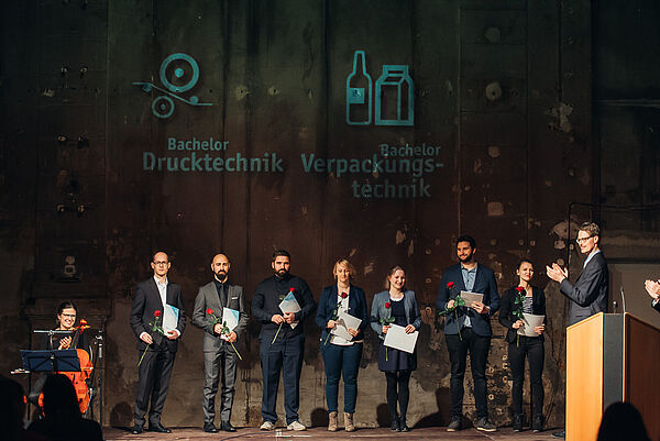 Eine Gruppe steht auf der Bühne mit Rose und Mappe in der Hand