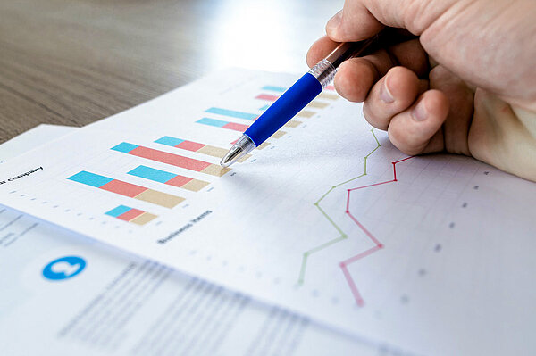 Blick auf Diagramme und Statistiken, eine Hand mit Kugelschreiber zeigt auf einen wichtigen Punkt