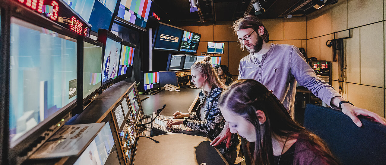 Studierende stehen vor Bildschirmen im Kontrollraum des Fernsehstudios