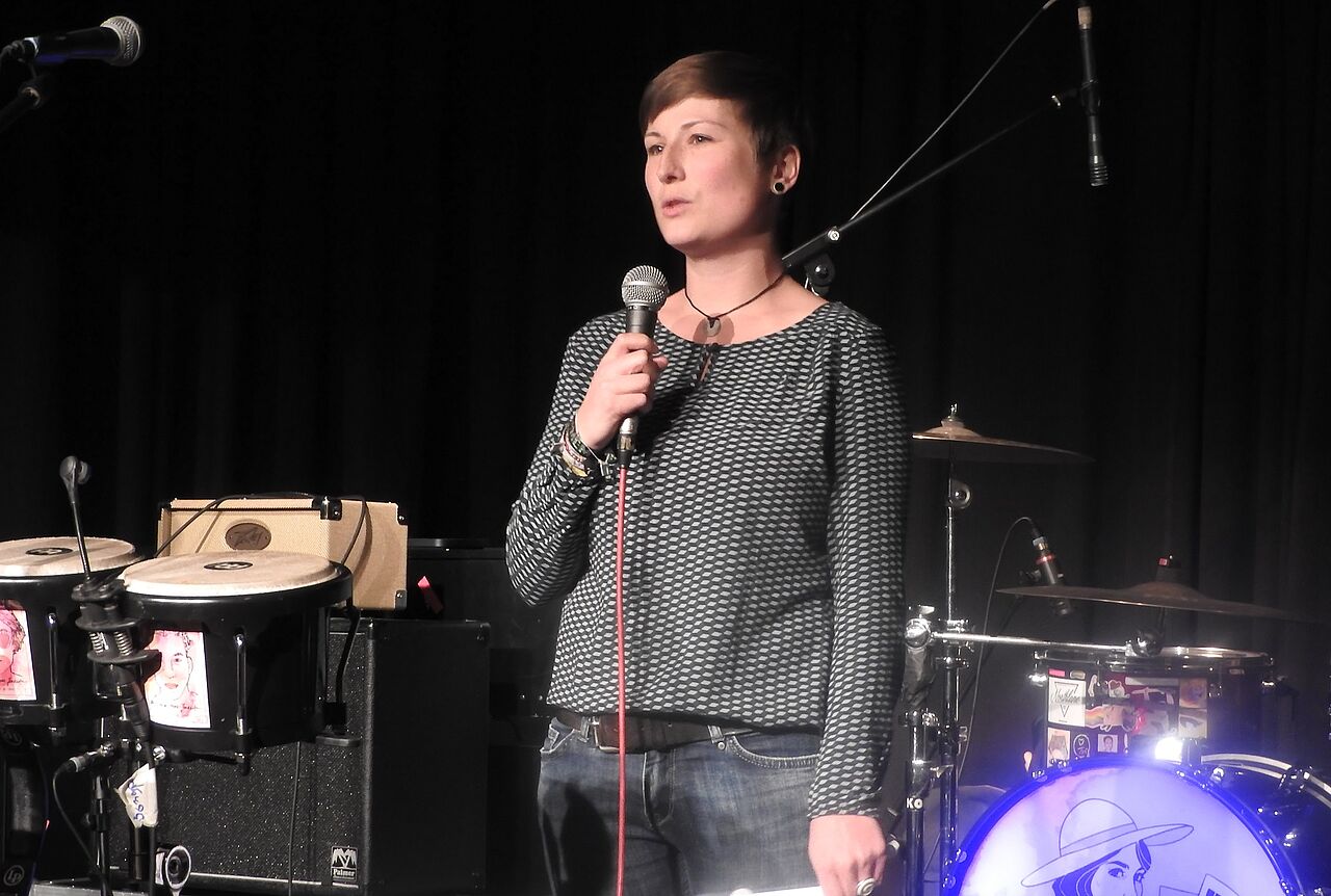 eine Frau spricht auf Bühne in ein Mikro