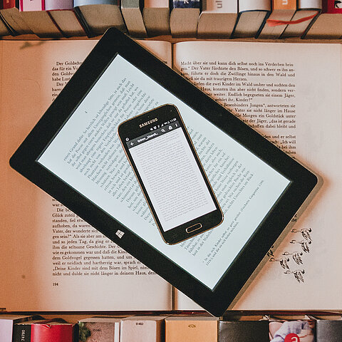 Bild zeigt ein iPhone, einen e-Reader und ein Buch übereinander gestapelt.