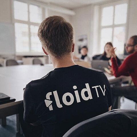 Bild zeigten einen Mann mit floidTV-T-Shirt an einem Tisch sitzend