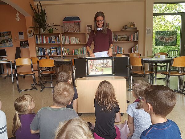 Eine Frau steht hinter einem kleinen Theater, davor sitzen Kinder