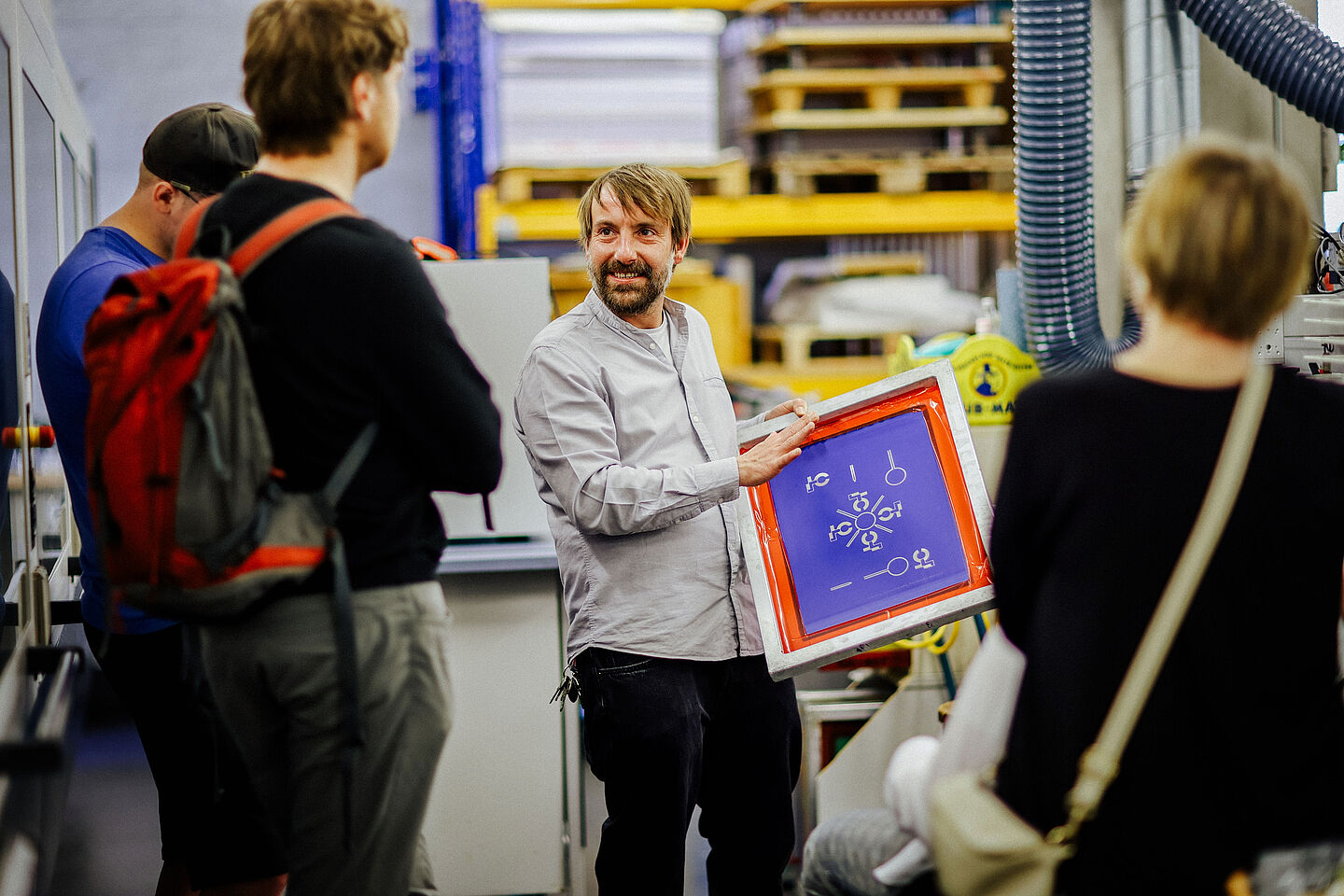 Prof. Ingo Reinhold zeigt eine beschichtete Oberfläche. (Foto: Anne Schwerin/HTWK Leipzig) Mann in der Mitte zeigt einer Gruppe eine bunte Tafel