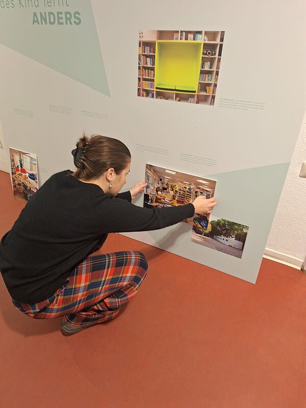 Ausstellung Studierende Schulmuseum junge Frau bringt Bild an Wand an