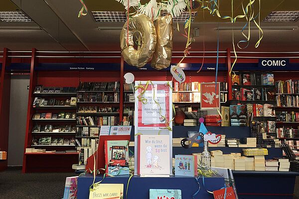 Auf einem Tisch sind Kinderbücher des Klett Kinderbuch Verlags ausgestellt. Über dem Tisch hängen bunte Girlanden und ein Luftballon in Form der Zahl Zehn