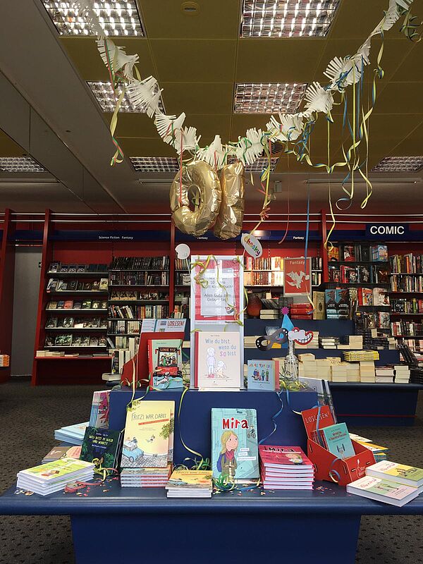 Auf einem Tisch sind Kinderbücher des Klett Kinderbuch Verlags ausgestellt. Über dem Tisch hängen bunte Girlanden und ein Luftballon in Form der Zahl Zehn