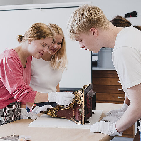 Bild zeigt 3 Personen wie sie ein Austellungsstück untersuchen.