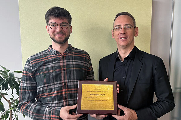 zwei Männer halten einen Award in den Händen