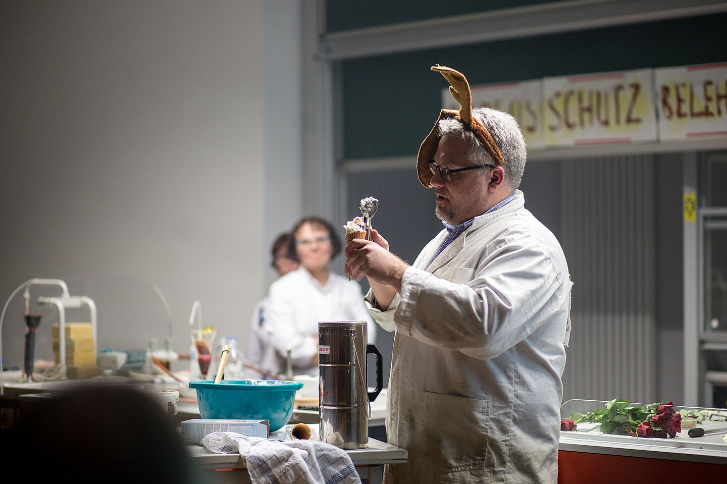 Lutz Engisch steht hinter dem Pult und hält eine Eiswaffel in der einen Hand, in die er mit der anderen Hand Stracciatella-Eiscreme füllt.