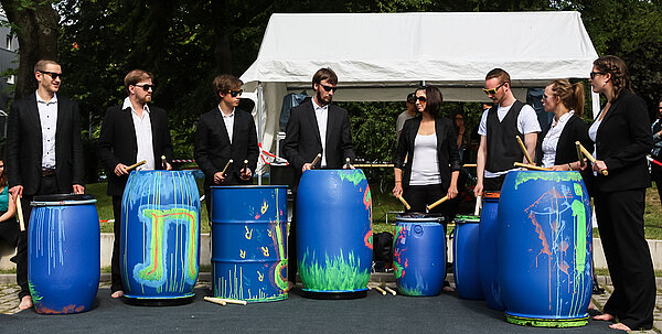 Mehrere Studenten im Anzug trommeln auf selbstgebauten Trommeln