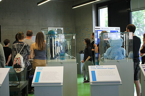 Viele Teilnehmer*innen bei der Führung zur Eröffnung der Ausstellung "Deep Blue Feelings" in der HTWK Bibliothek sind von hinten abgebildet und betrachten Vitrinen