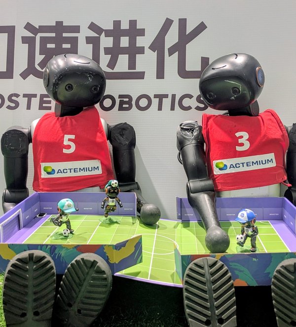 zwei humanoide Roboter sitzen nebeneinander vor einer Wand mit chinesischen Schriftzeichen