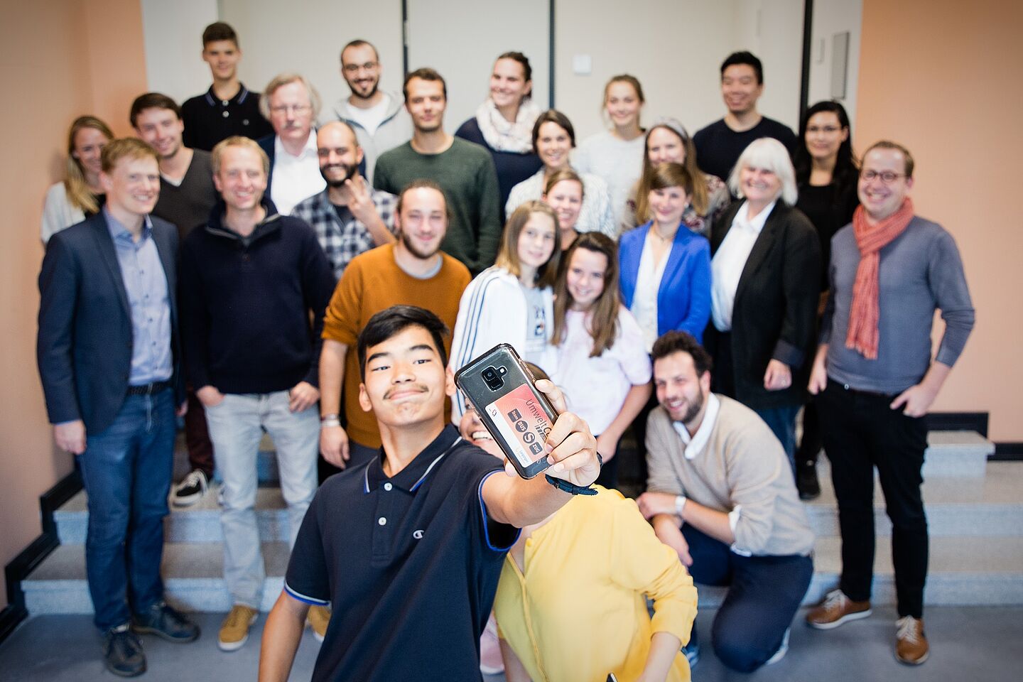 Gruppenbild, im Vordergrund ein junger Mann mit Smartphone