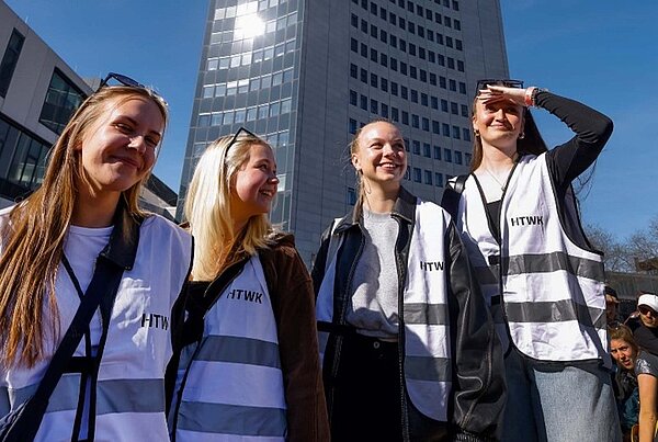 Vier Studierende der HTWK, die Hochschul-Westen tragen, zum Team der Fakultät gehören und vor der Moritzbastei stehen, , sichten die Lage. 