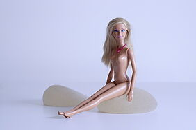 Barbiepuppe sitzt auf Silikonimplantaten