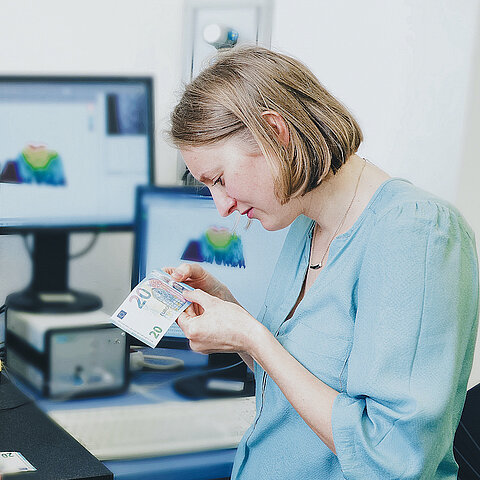 Bild zeigt eine Frau wie sie einen 20-Euro-Schein untersucht.