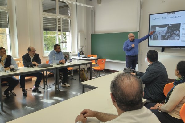 Personen in Seminarraum lauschen Vortrag