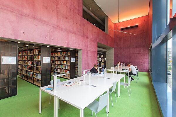 Drei Personen sitzen mit Abstand an Tischen in der Bibliothek.