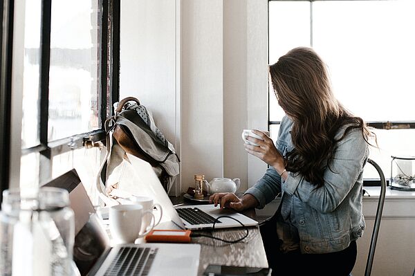 junge Frau sitzt im Cafe mit Kaffee in der Hand am Laptop