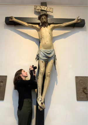 Ein bewegliches Kruzifix mit einer Skulptur von Christus. Daneben eine Frau, die das Kunstwerk fotografiert.