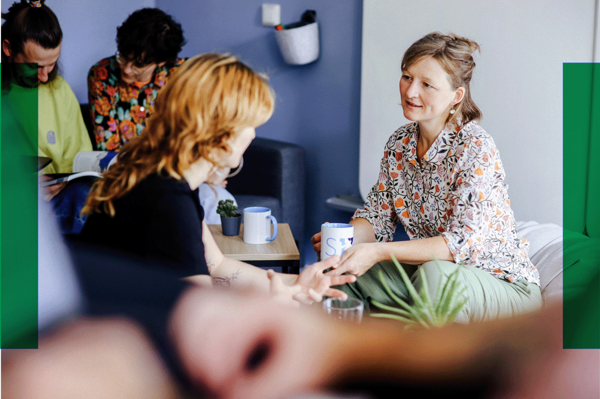 Fünf Personen sitzen in einem hellen Raum, unterhalten sich und trinken Kaffee. Zwei Frauen sprechen sich direkt gegenüber.. Zur Seite Unterstützung auf Augenhöhe mit Ment4Science.