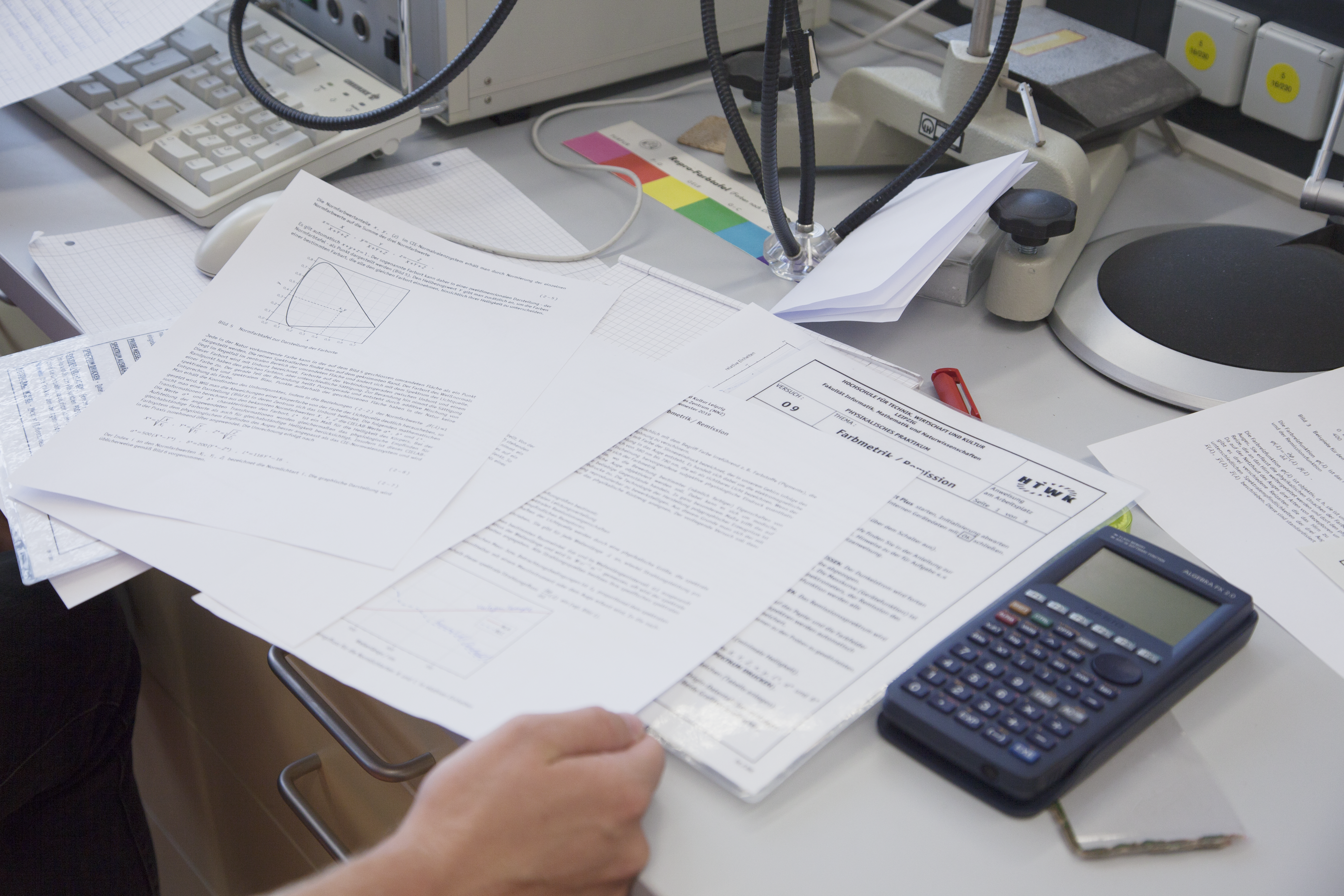 Arbeitsplatz auf dem Arbeitsblätter mit physikalischen Aufgaben sowie ein Taschenrechner liegen.