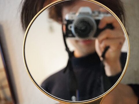 Ein Handspiegel ist in Detailaufnahme zu sehen. Im Spiegelbild ist der Fotograf zu sehen