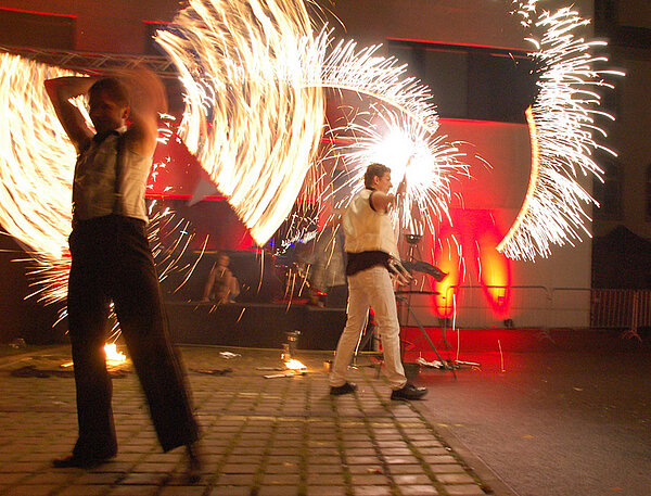 Zwei Artisten führen eine Feuershow vor dem Gebäude der Medienfakultät vor