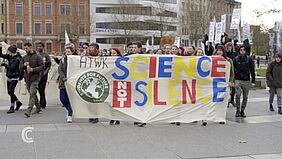 Screenshot der Campus Compact-Sendung zur Klimastreikwoche: Menschen laufen auf der Straße und ragen ein Soffplakat mit der Auschrift „HTWK Students for future Science not silence“ 