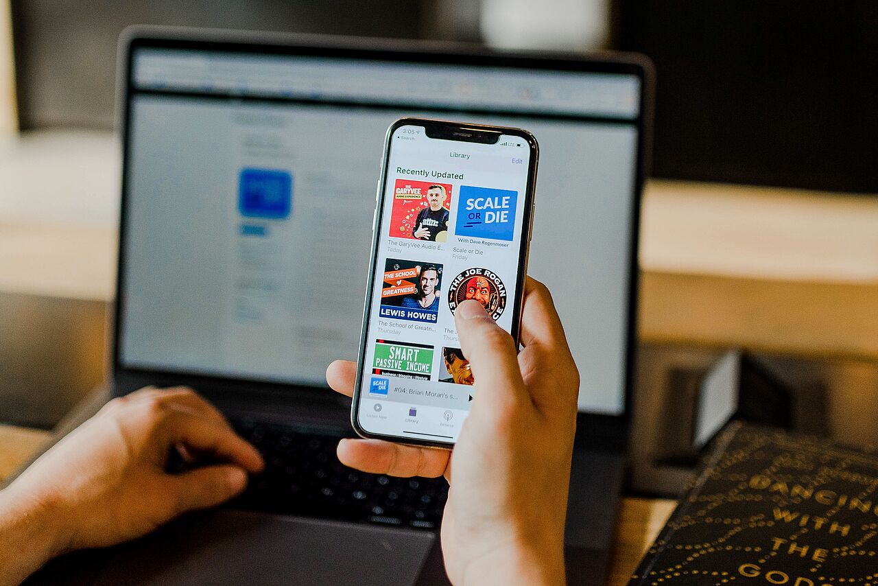 unbekannte Person, die vor einem Notebook sitzt und ein Smartphone in der Hand hält