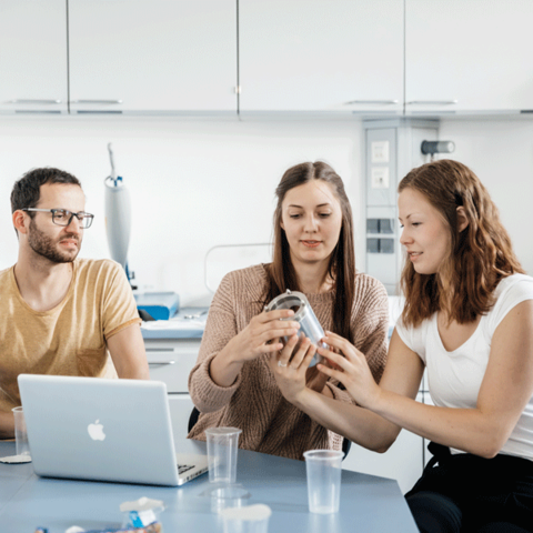 Bild zeigt 3 Personen an einem Tisch wie sie eine Verpackung untersuchen.