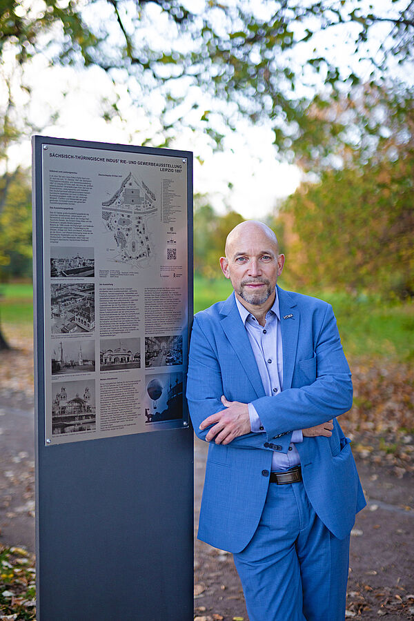 STIGA Stele Dr. Ruge steht im blauen Anzug neben einer Stele im Clara-Zetkin-Park