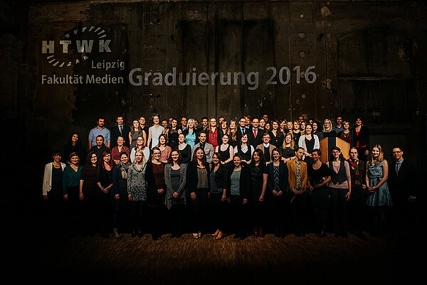 Die gesammelten Graduierten der Fakultät Medien posieren auf der Bühne für ein Gruppenbild