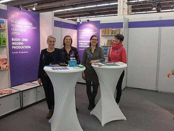 Die Kommilitoninnen der Studiengänge Buch- und Medienproduktion und Buchhandel/Verlagswirtschaftstehen gemeinsam an ihrem Stand auf der Frankfurter Buchmesse