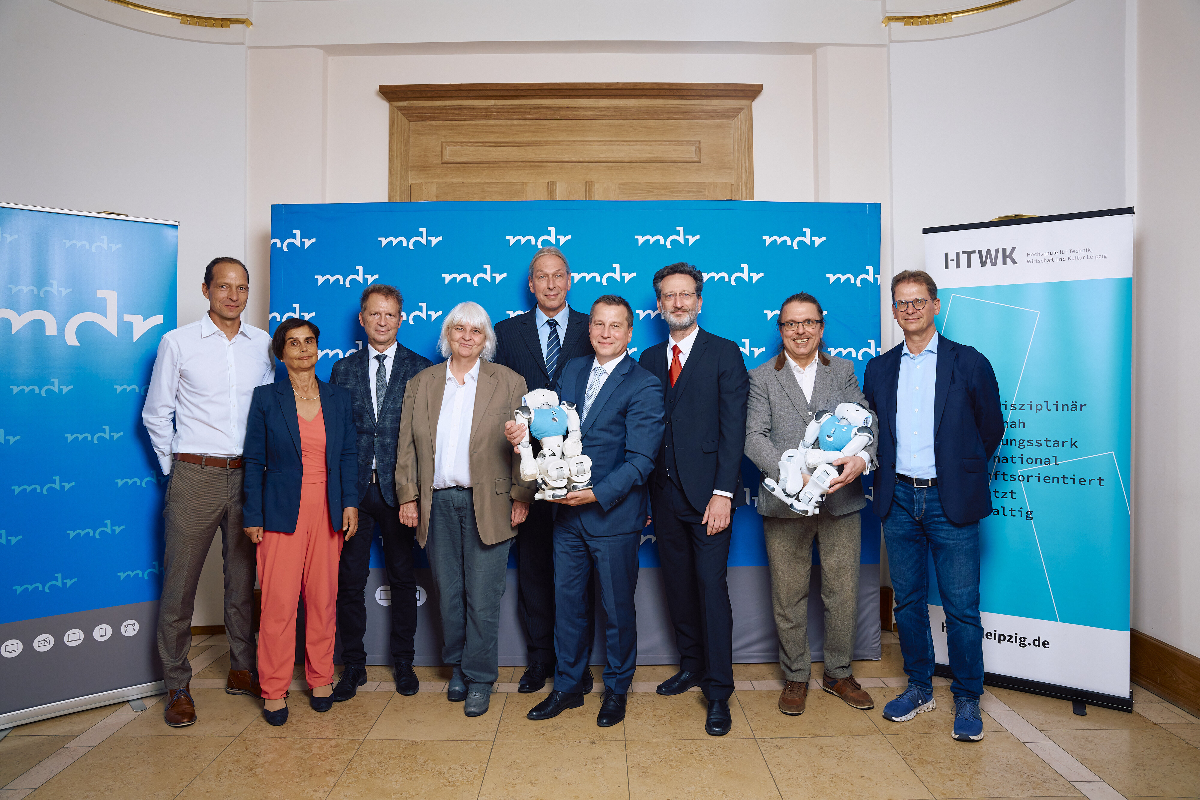 Gruppe von neun Personen mit zwei Robotern vor Schmuckwand