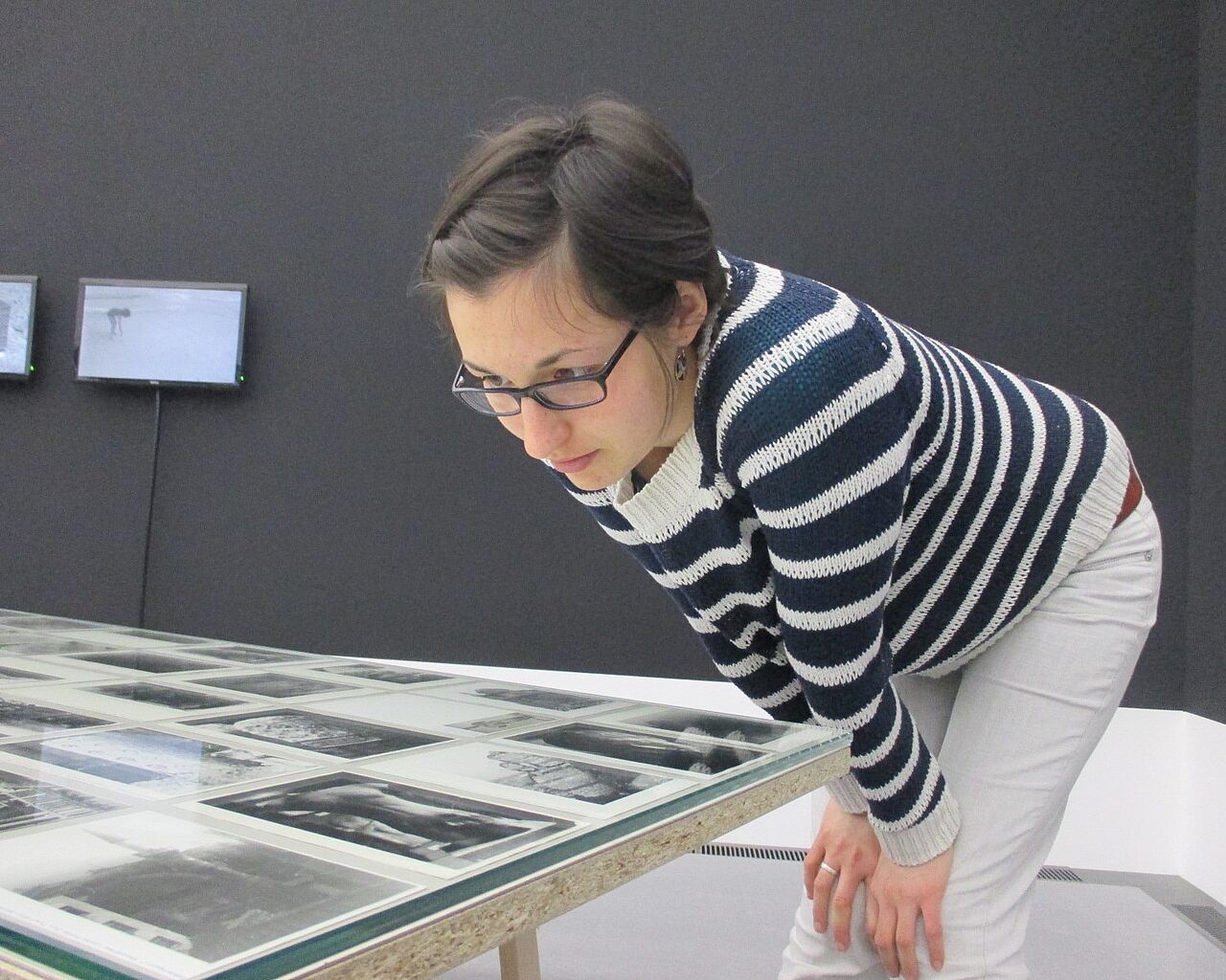 Eine Absolventin des Studiengangs Museologie an der HTWK Leipzig betrachtet Fotos, die auf einem Tisch in einer Museumsausstellung liegen.