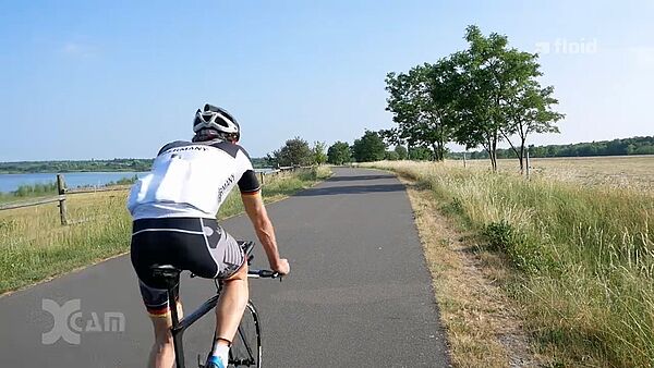 Screenshot einer Sendung von floid: Mann in Rennradkleidung auf Rennrad am See