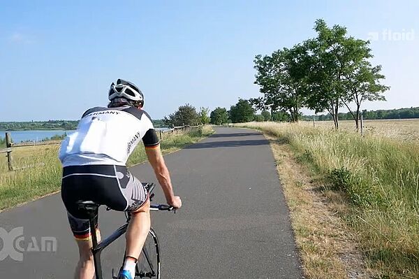 Screenshot einer Sendung von floid: Mann in Rennradkleidung auf Rennrad am See