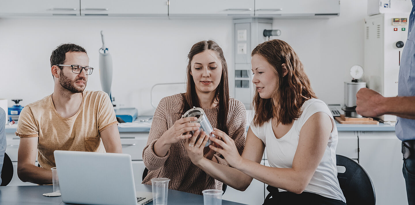 Studierende untersuchen am Tisch einen Verpackungsgegenstand