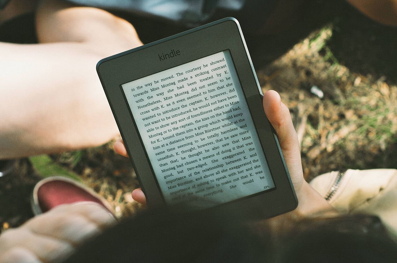 unbekannte Person blickt auf Ebookreader und liest einen Text im Freien