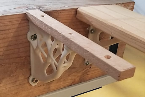 Nahaufnahme eines dunklen Elementes mit schmaler Regalauflage an einem Holzblock befestigt