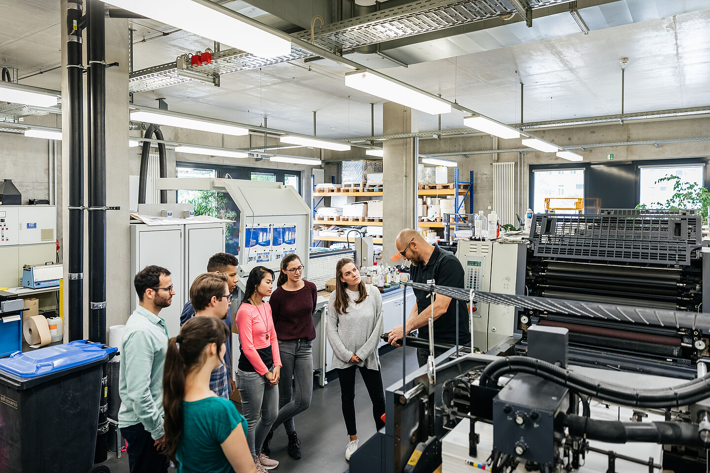 Eine lehrende Person zeigt einer Gruppe Studierender die Bedienung einer Maschine im Drucksaal der HTWK Leipzig.