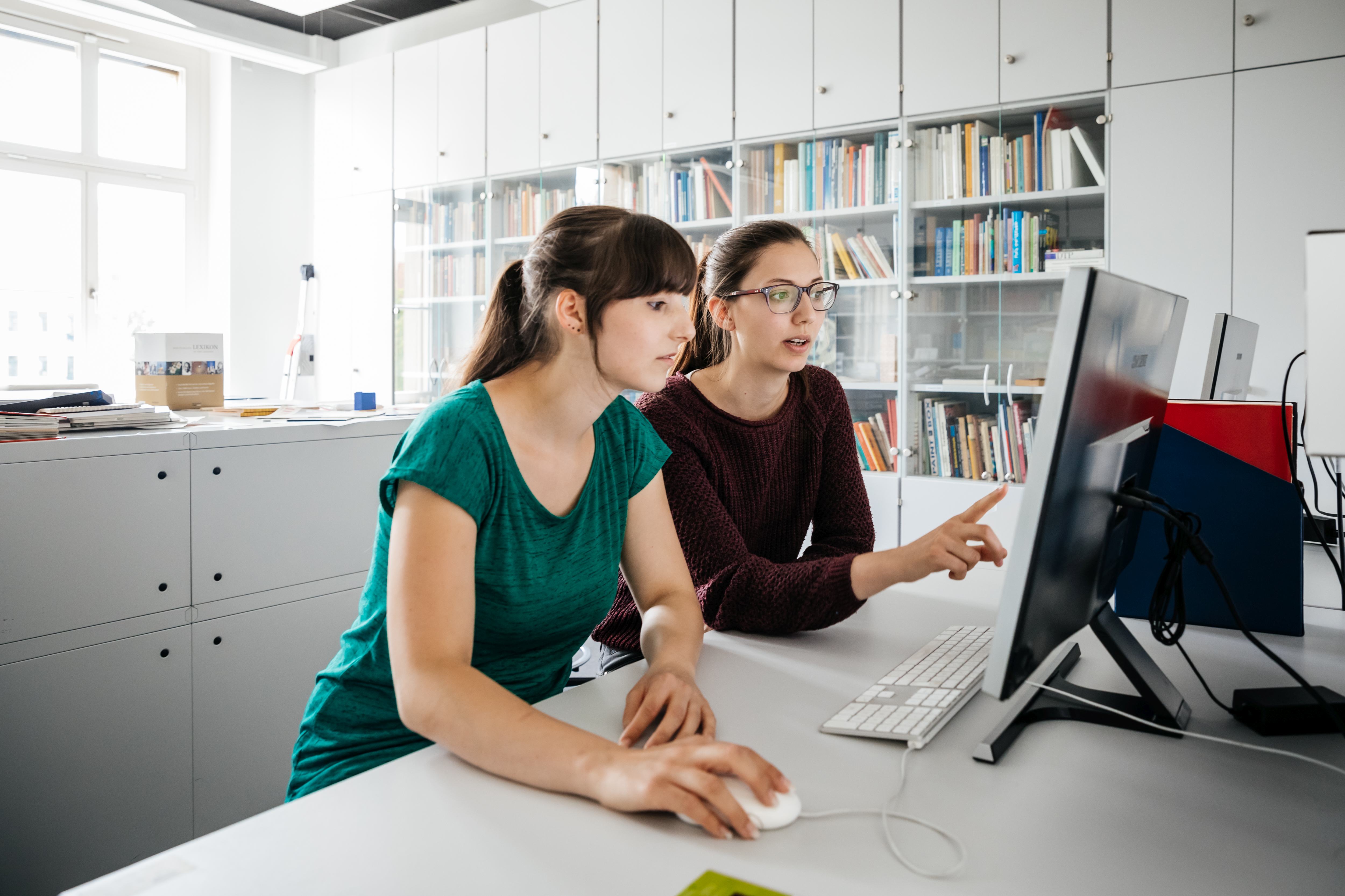 Zwei Personen schauen gemeinsam auf einen Computermonitor in einem hellen Büro.