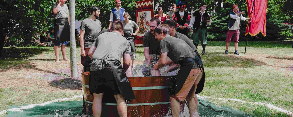 Fünf Männer tauchen einen Studienkollegen in ein, mit kaltem Wasser gefülltes Fass.