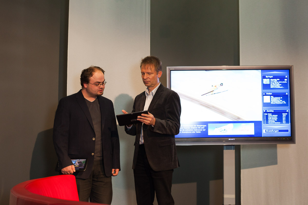 zwei Männer auf einer Bühne erläutern Casual TV mit Tablett in der Hand