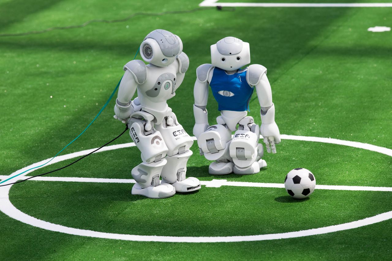 zwei kleine Roboter auf einem grünen Rasen, die gegeneinander Fußball spielen